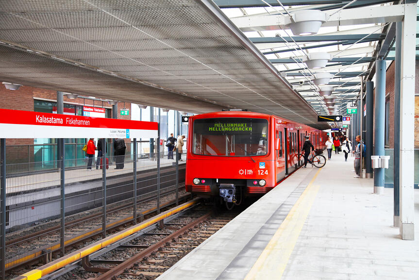 Kalasataman metroaseman laiturilla seisoo oranssi metrojuna, jonka ovilla on muutamia matkustajia