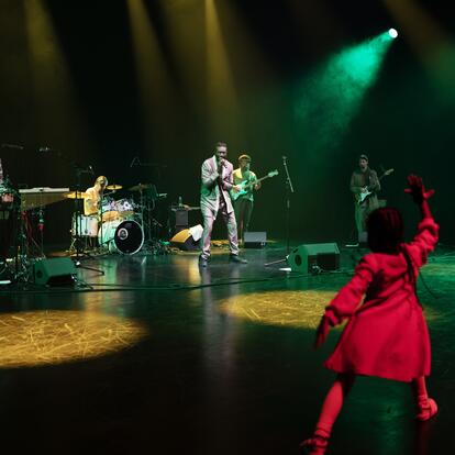 A band playing in a dark room and a child dancing in the front. 
