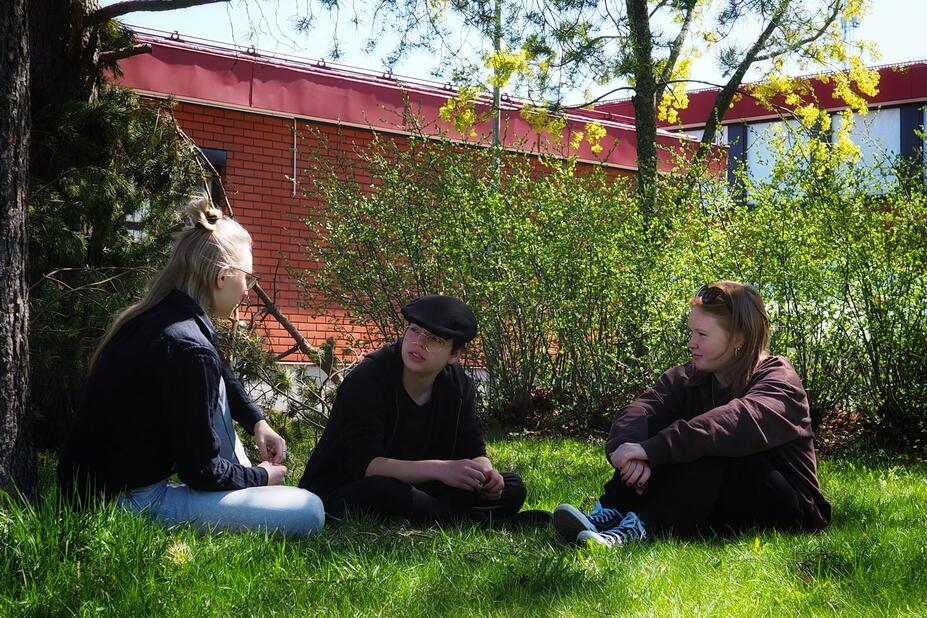 Opiskelijoita istumassa koulun pihassa puun alla