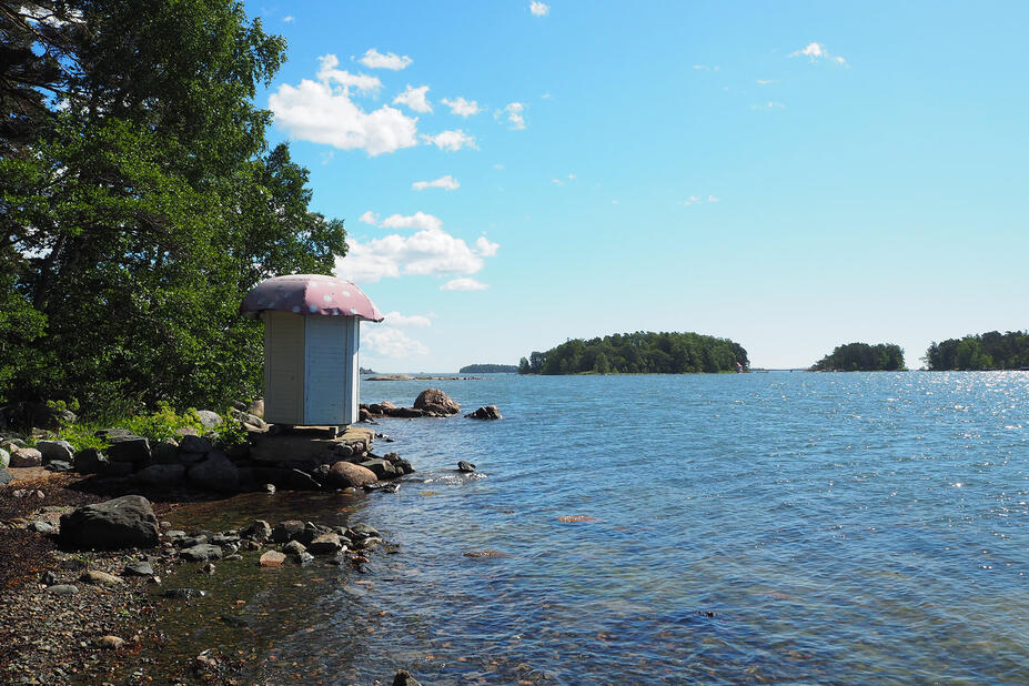 Kivisellä rannalla uimakoppi, meri ja puita.