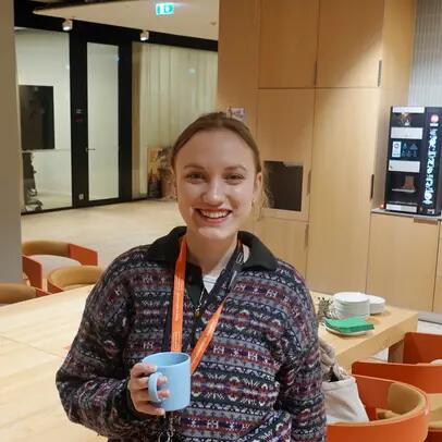 Korkeakouluharjoittelija Katia toimiston kahvihuoneessa kahvikuppi kädessään.