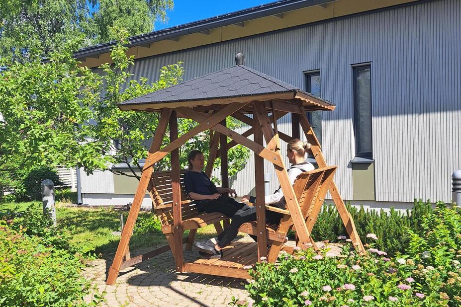 Two people are sitting on a swing in a summer yard.